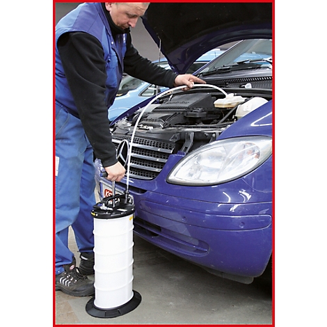 Ein Mechaniker mit Overall und offener Motorhaube arbeitet an einem blauen Auto. Er hält einen weißen Behälter mit einem Schlauch.